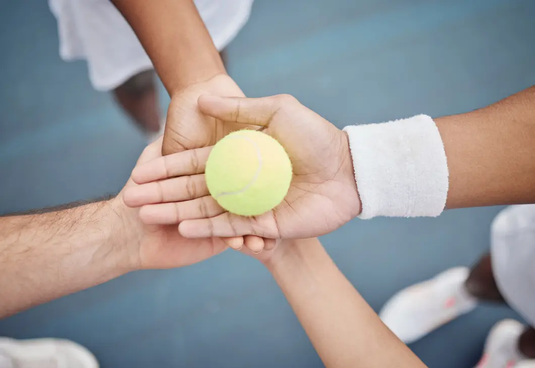 Vier Hände halten gemeinsam einen Tennisball
